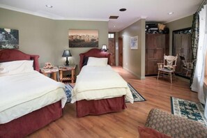 Een hotelkamer met twee bedden, houten vloeren, een zithoek met een stoel en een kledingkast.