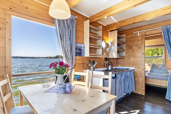 A cabin with a wooden interior, a dining area, a kitchen, and a view of a lake.