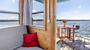 A cabin with a view of the water, a wooden deck, a table with a vase, and a red pillow. - Houseboat BunBo 1060 - Do (Königs Wusterhausen OT Zernsdorf)