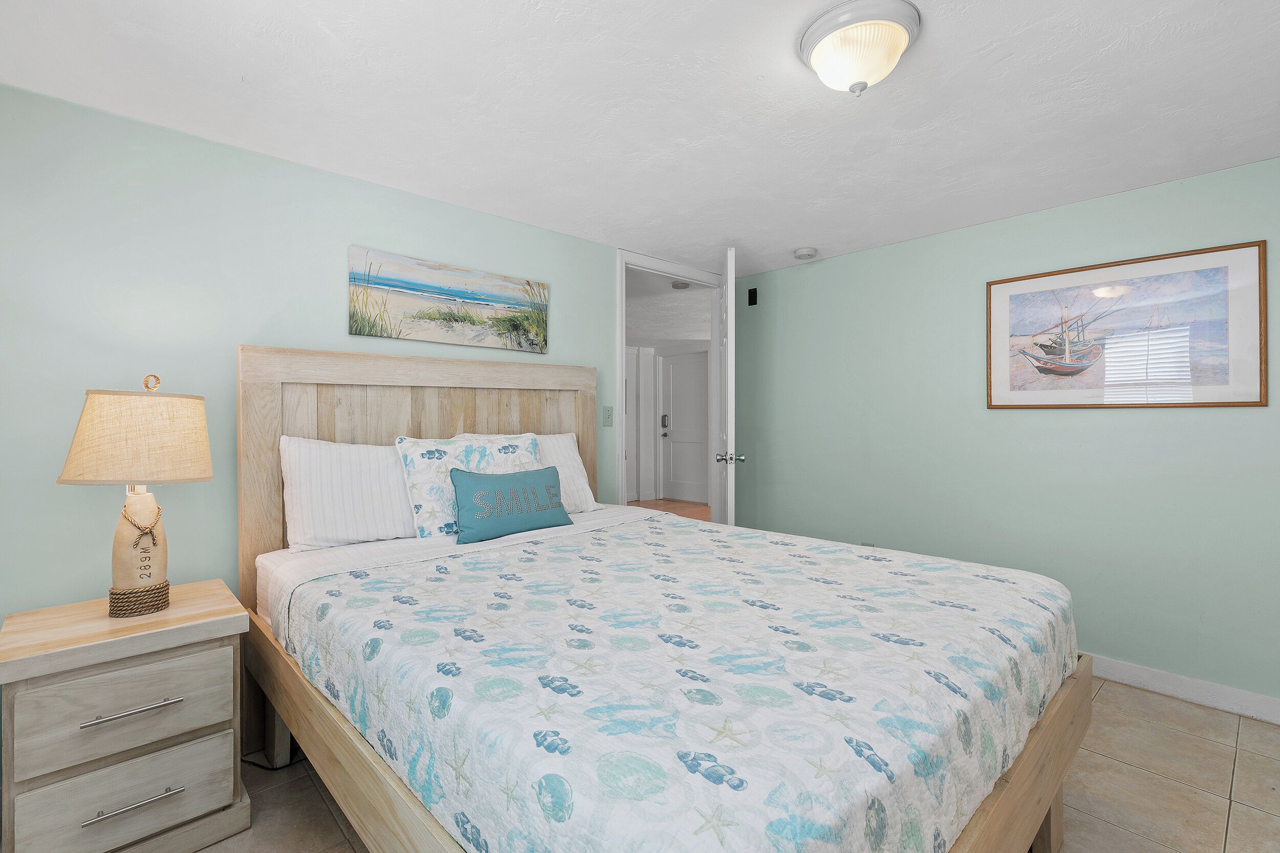 A bedroom with a bed, a nightstand, a lamp, and two framed pictures on the wall.