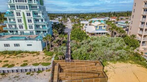 A coastal hotel with multiple floors, a pool, and a beach area with wooden structures.