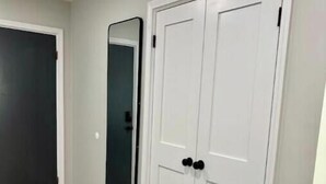 Un pasillo con suelo de madera, una puerta blanca con manijas negras y un espejo grande en la pared.