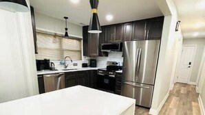 Una cocina moderna con encimera blanca, electrodomésticos de acero inoxidable y taburetes de madera.