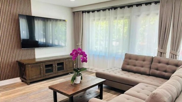 Una sala moderna con un televisor de pantalla plana grande, un sofá marrón, una mesa de centro de madera y una orquídea en maceta.
