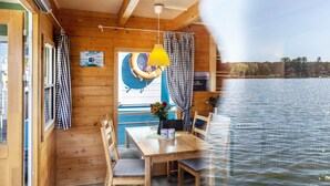 En hytte med træpaneler, et bord med stole, en hængende lampe og udsigt over vandet.