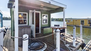 En overdækket terrasse med siddepladser, et lille bord og udsigt til vandet.