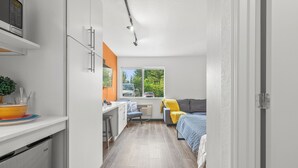 Une pièce compacte comprenant un coin cuisine, un lit, un bureau et une fenêtre donnant sur l’extérieur.