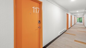 Un couloir d’hôtel avec des portes orange, des murs blancs et un sol recouvert de moquette.