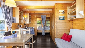 Et sommerhusinteriør med træpaneler, et spisebord, en sofa og udsigt gennem et vindue.