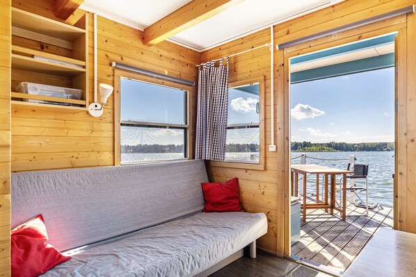 A wooden cabin with a sofa, a table, and a view of a lake.