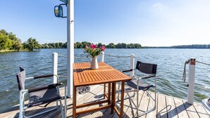 En træterrasse med et bord og stole, en potteplante og udsigt til en sø.