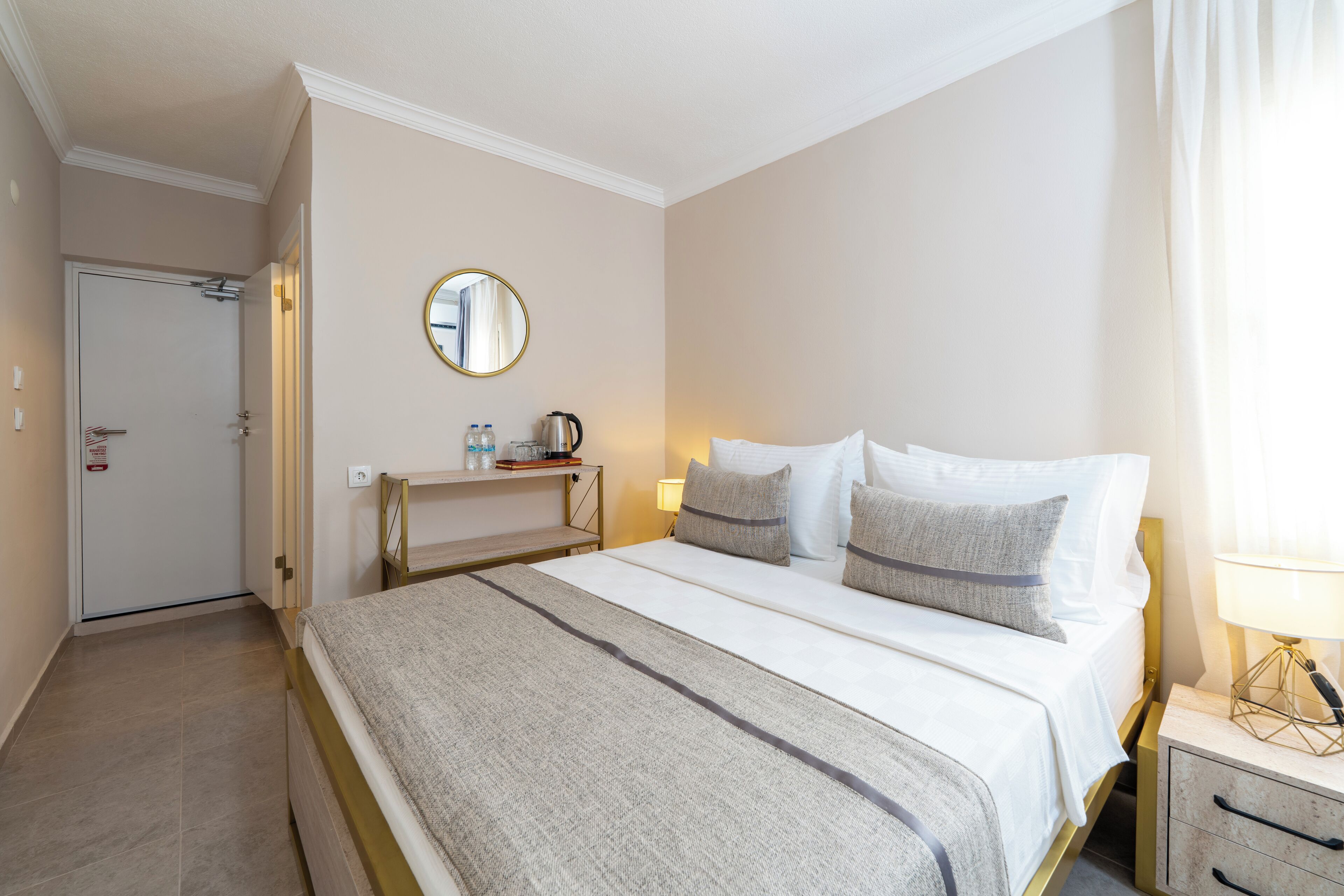 A hotel room with a bed, bedside table, lamp, and a mirror on the wall.