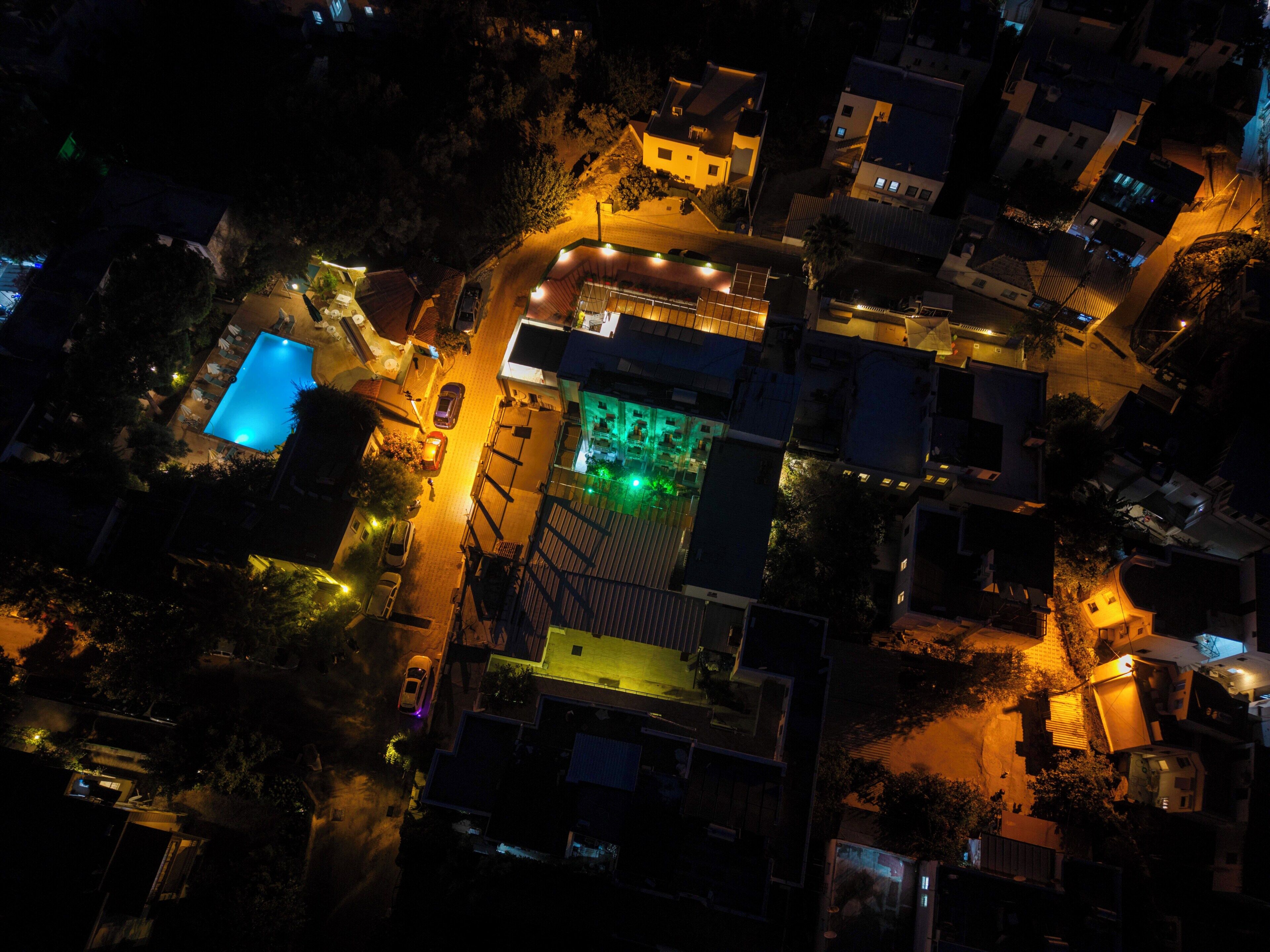 An aerial view of a residential area with houses, a swimming pool, and a green-lit building.