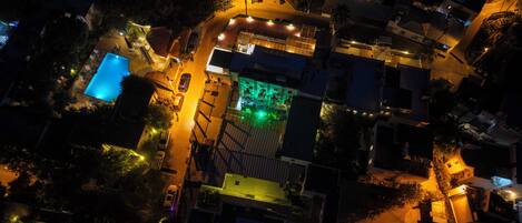 An aerial view of a residential area with houses, a swimming pool, and a green-lit building.