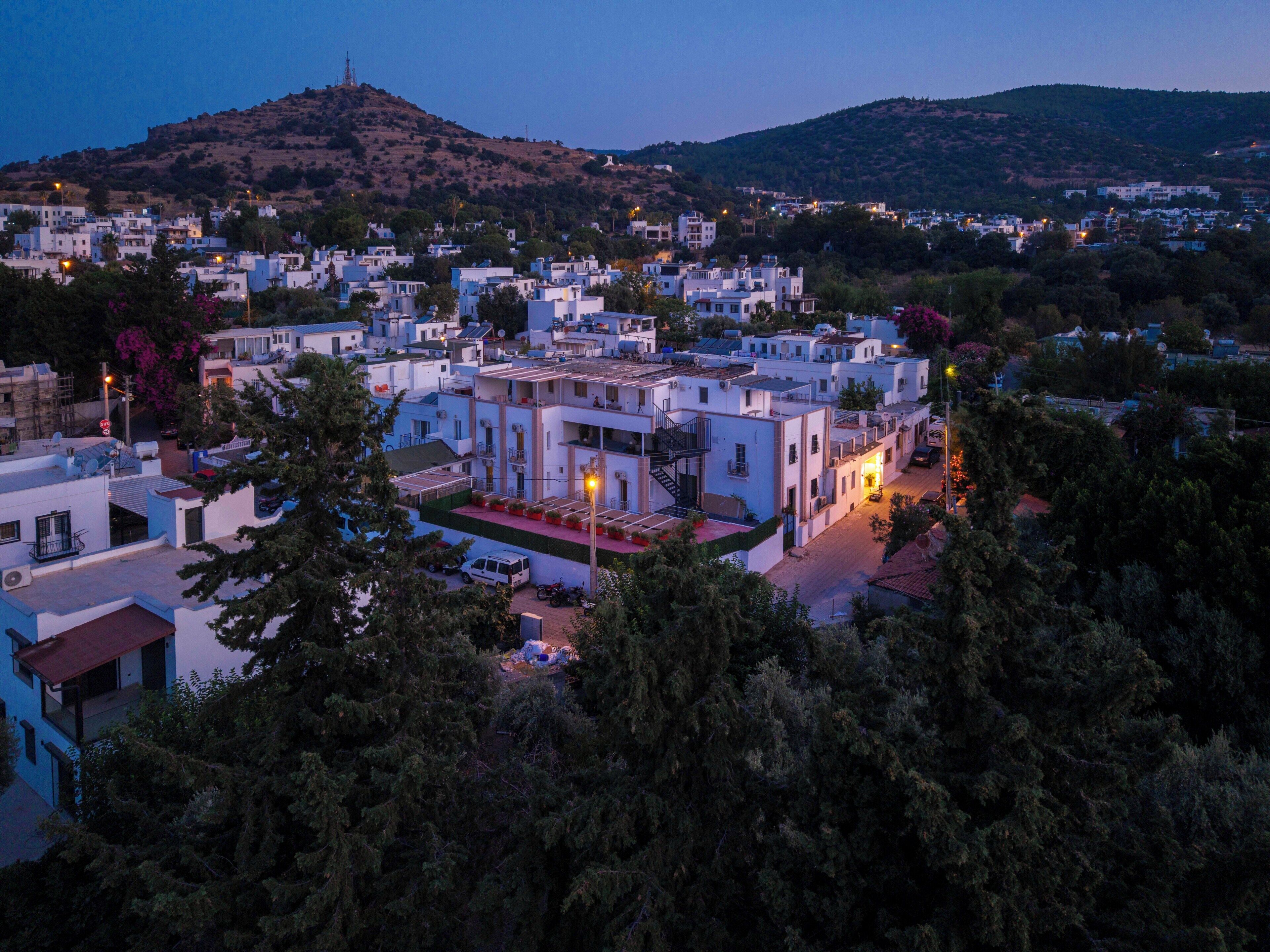 A residential area with white buildings, a hill in the background, and trees in the foreground.