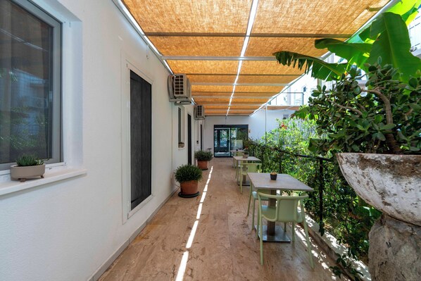 Un pasillo con ventilador de techo, plantas en macetas y zona de estar exterior.