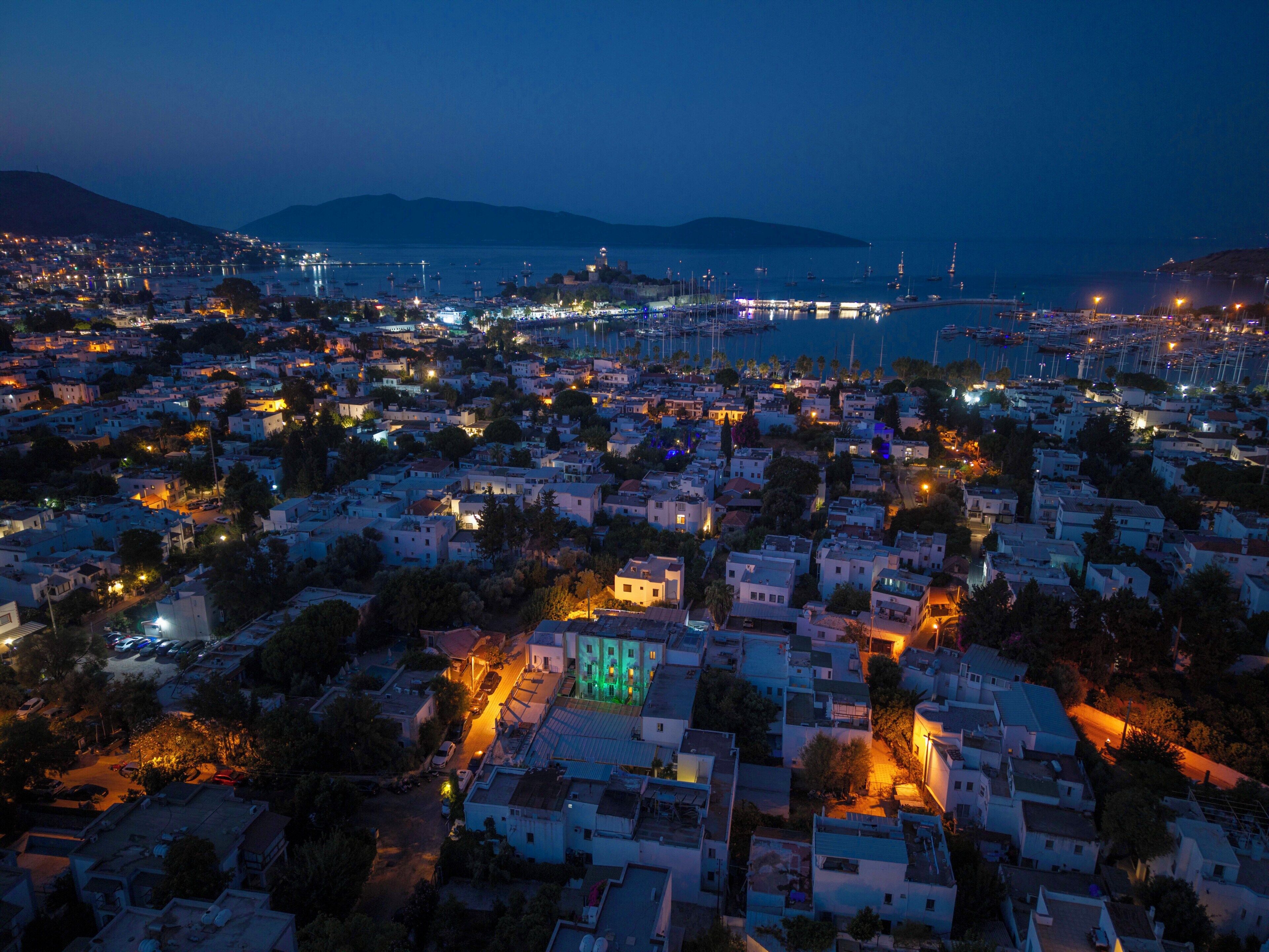 An aerial view of a coastal town at dusk with buildings, roads, and a marina.