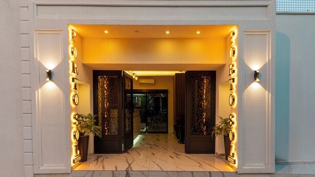 Entrada de hotel con letreros iluminados y plantas en macetas.