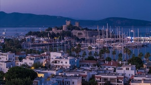 Un pueblo costero con un castillo histórico, un puerto deportivo con barcos y edificios residenciales.