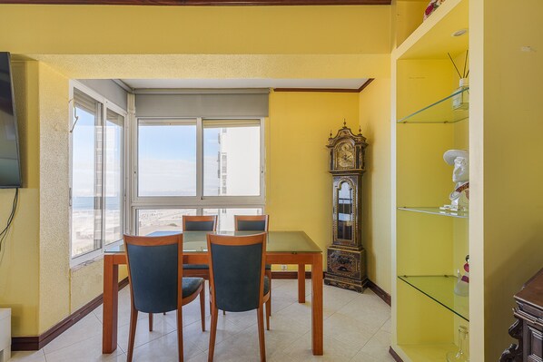 A dining area with a table and chairs, a large window, and a tall grandfather clock.