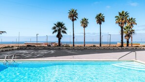 A swimming pool with a clear view of the beach and palm trees in the background. - T2 with Pool in Front of the Beach (Costa da Caparica)