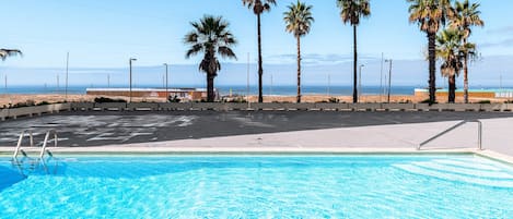 A swimming pool with a clear view of the beach and palm trees in the background.