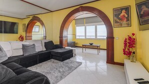 A living room with a sectional sofa, a coffee table, and a TV mounted on the wall. - T2 with Pool in Front of the Beach (Costa da Caparica)