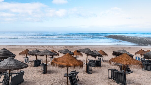 A beach with thatched umbrellas and chairs, a clear sky, and the ocean in the background. - T2 with Pool in Front of the Beach (Costa da Caparica)