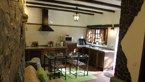 A cozy kitchen with a dining area, stone wall, and a green rug.