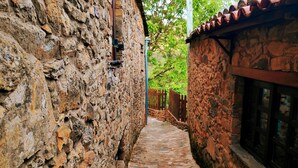 A narrow stone pathway flanked by rustic stone walls, leading to a wooden door and a window with a stone facade.