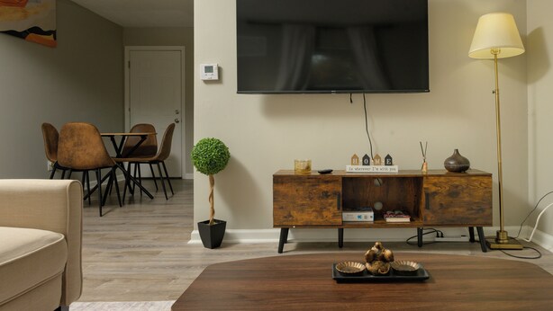 Ein modernes Wohnzimmer mit Flachbildfernseher, Couchtisch aus Holz, einer Couch, einem Esstisch mit Stühlen und einem Blumentopf.