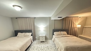 Ein Zweibettzimmer mit zwei Betten, einem Nachttisch, einem gemusterten Teppich und einer Deckenleuchte.