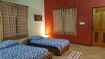 A room with two beds, a wooden door, and a wall with a geometric painting.