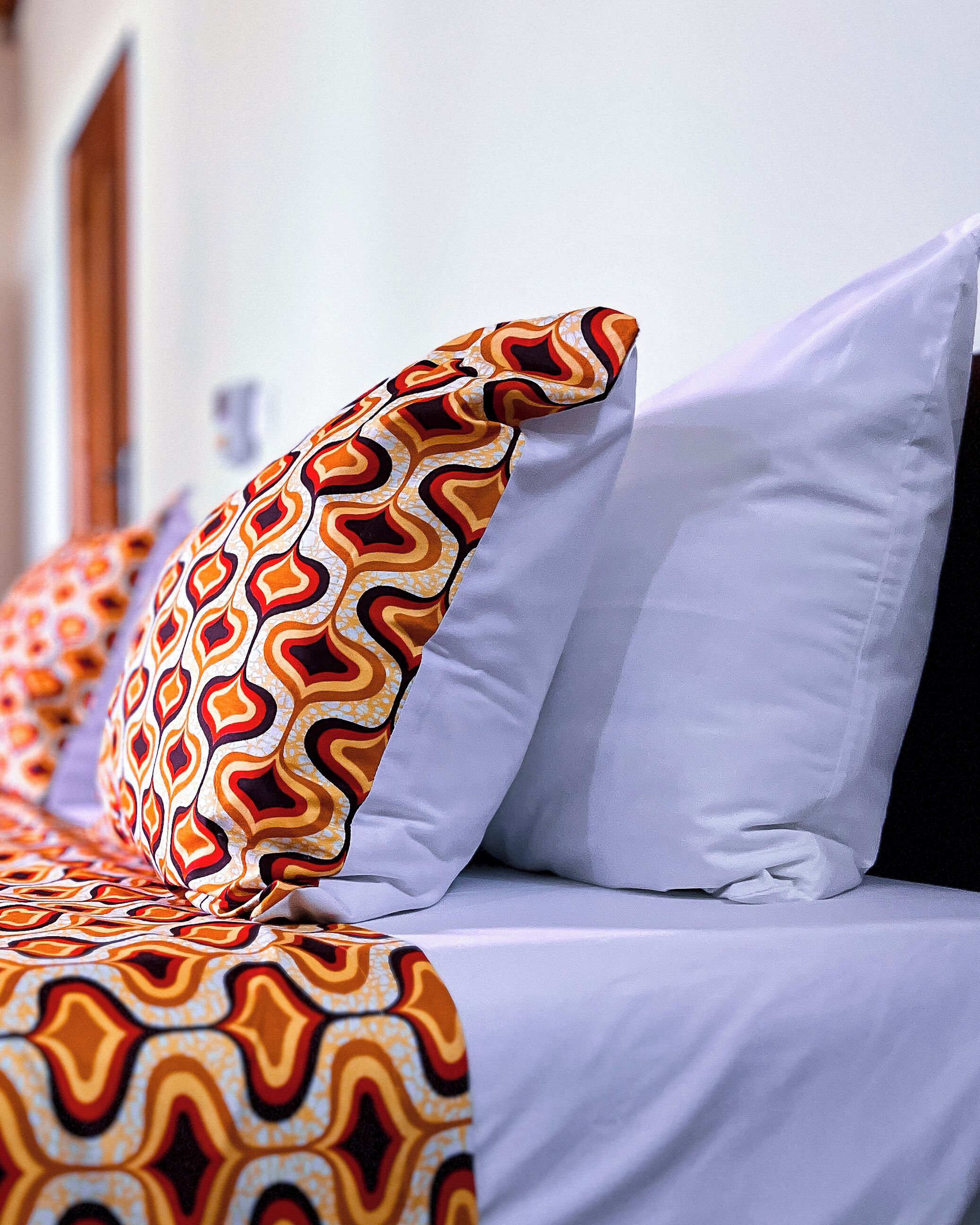 Una cama con almohadones estampados y una almohada blanca lisa.