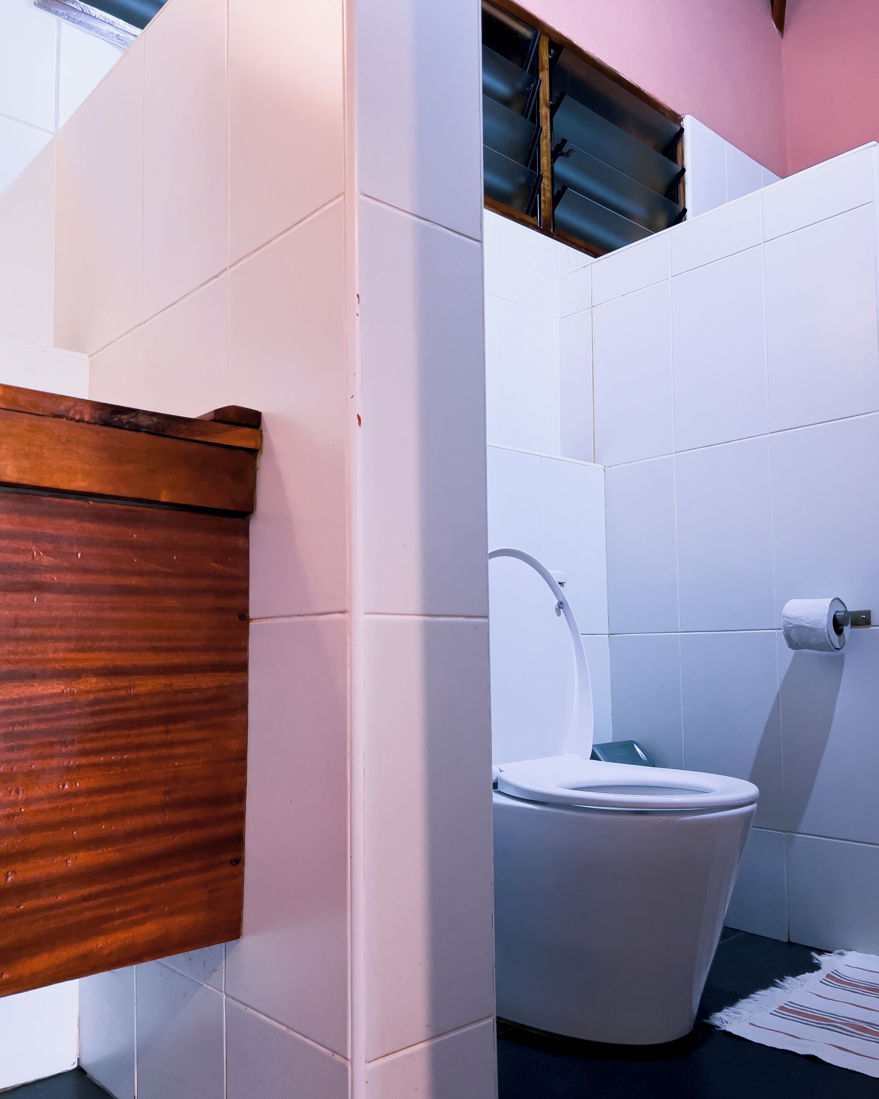 Un baño con azulejos blancos, un mueble de tocador de madera, un inodoro blanco y un perchero para toallas.