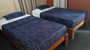 Dos camas individuales con cubrecamas estampados en una habitación con piso de madera y paredes color beige.