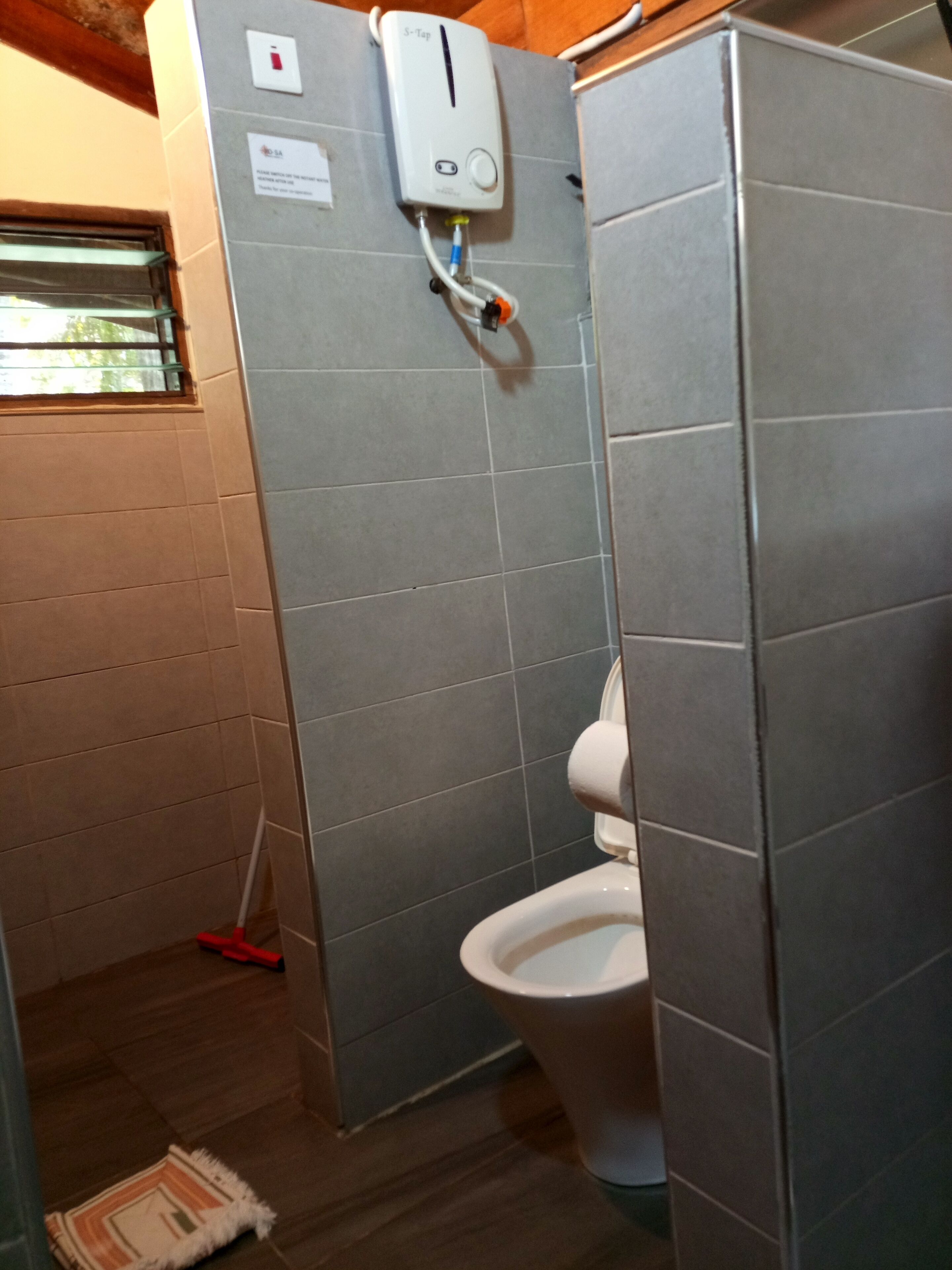 A bathroom with a toilet, a hand dryer, and a mop leaning against the wall.