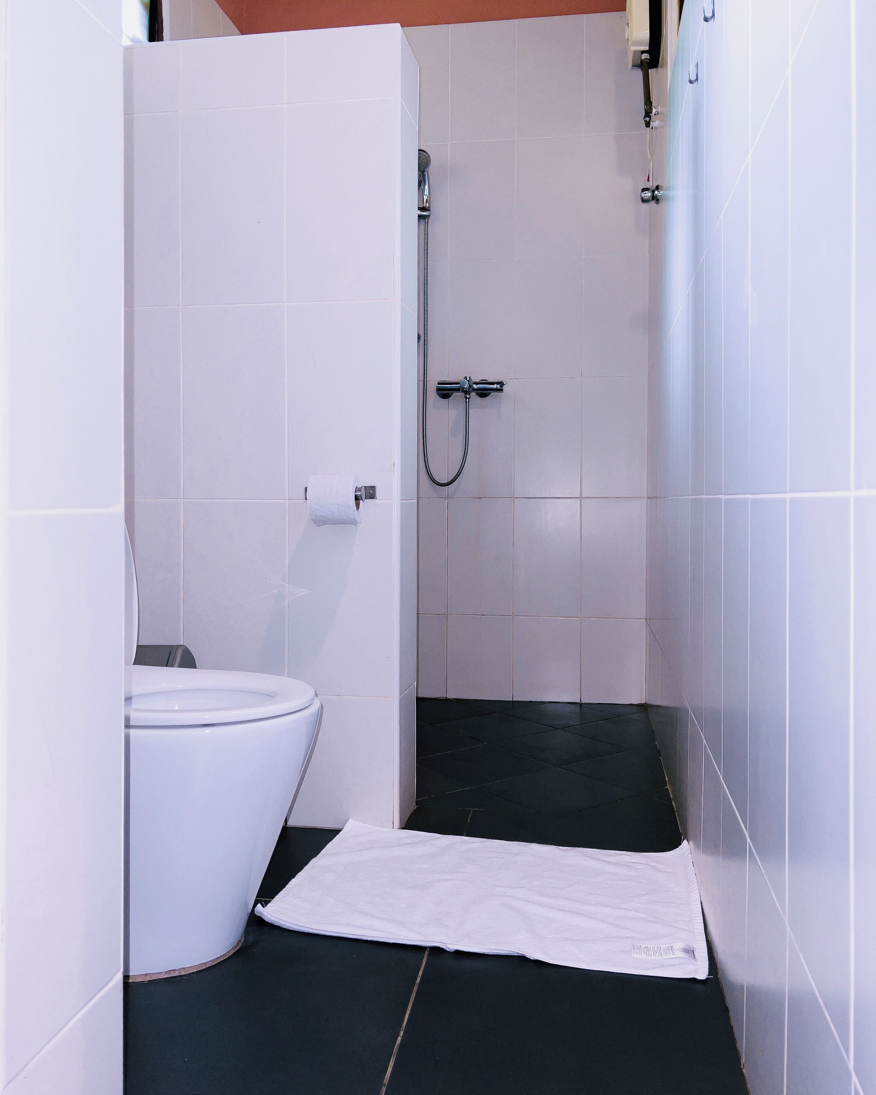 A small bathroom with a toilet, a shower, and a towel on the floor.