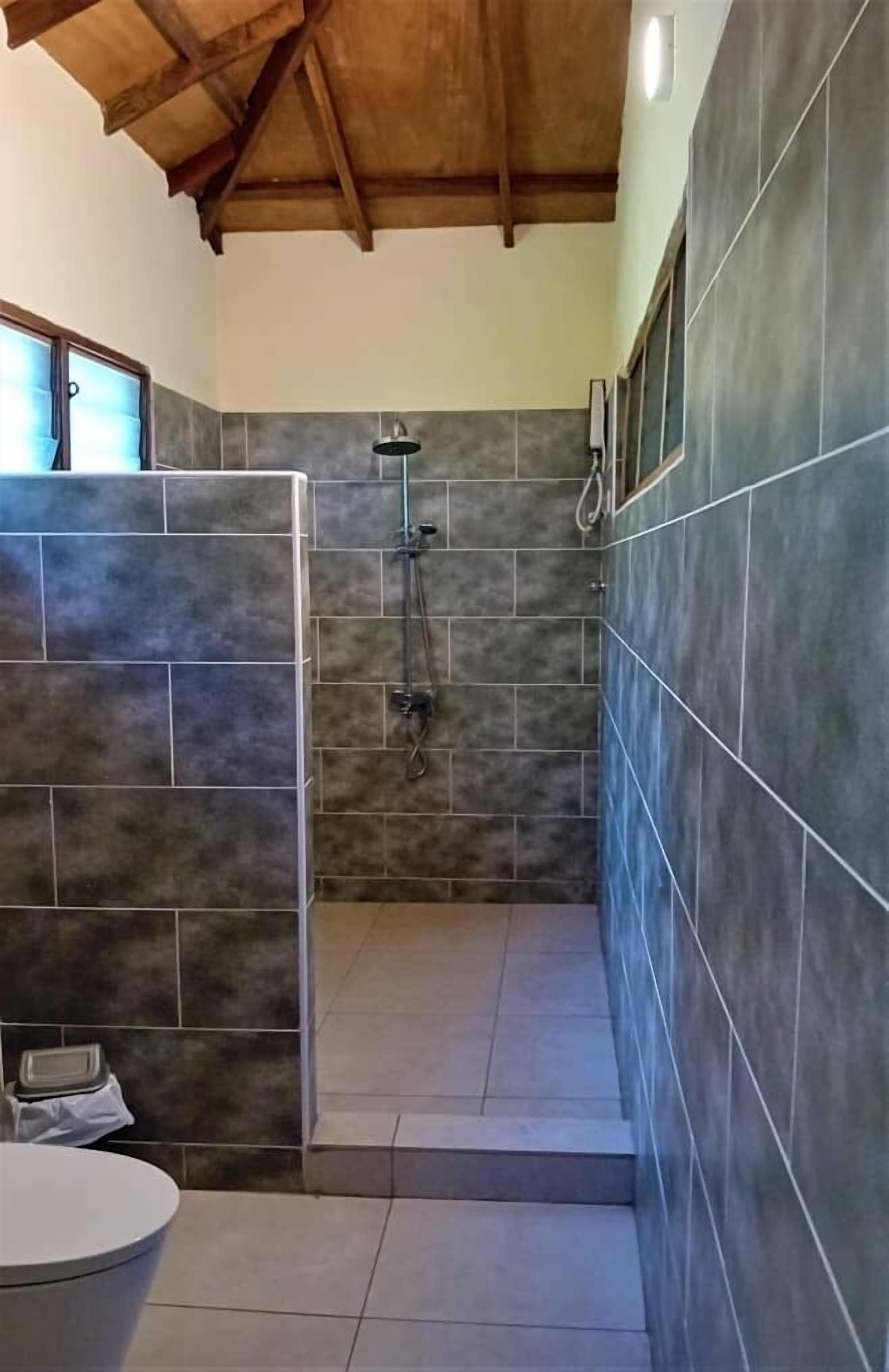 Une salle de bain avec une douche, des murs carrelés et un plafond en bois.