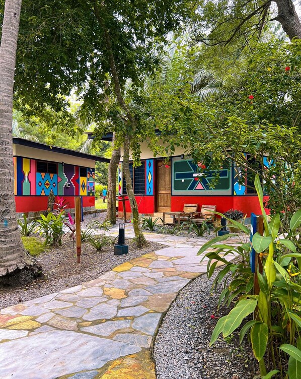 A colorful outdoor area with a stone pathway, a small seating area, and a building with vibrant murals. - Ko-Sa Beach Resort (Ampenyi)