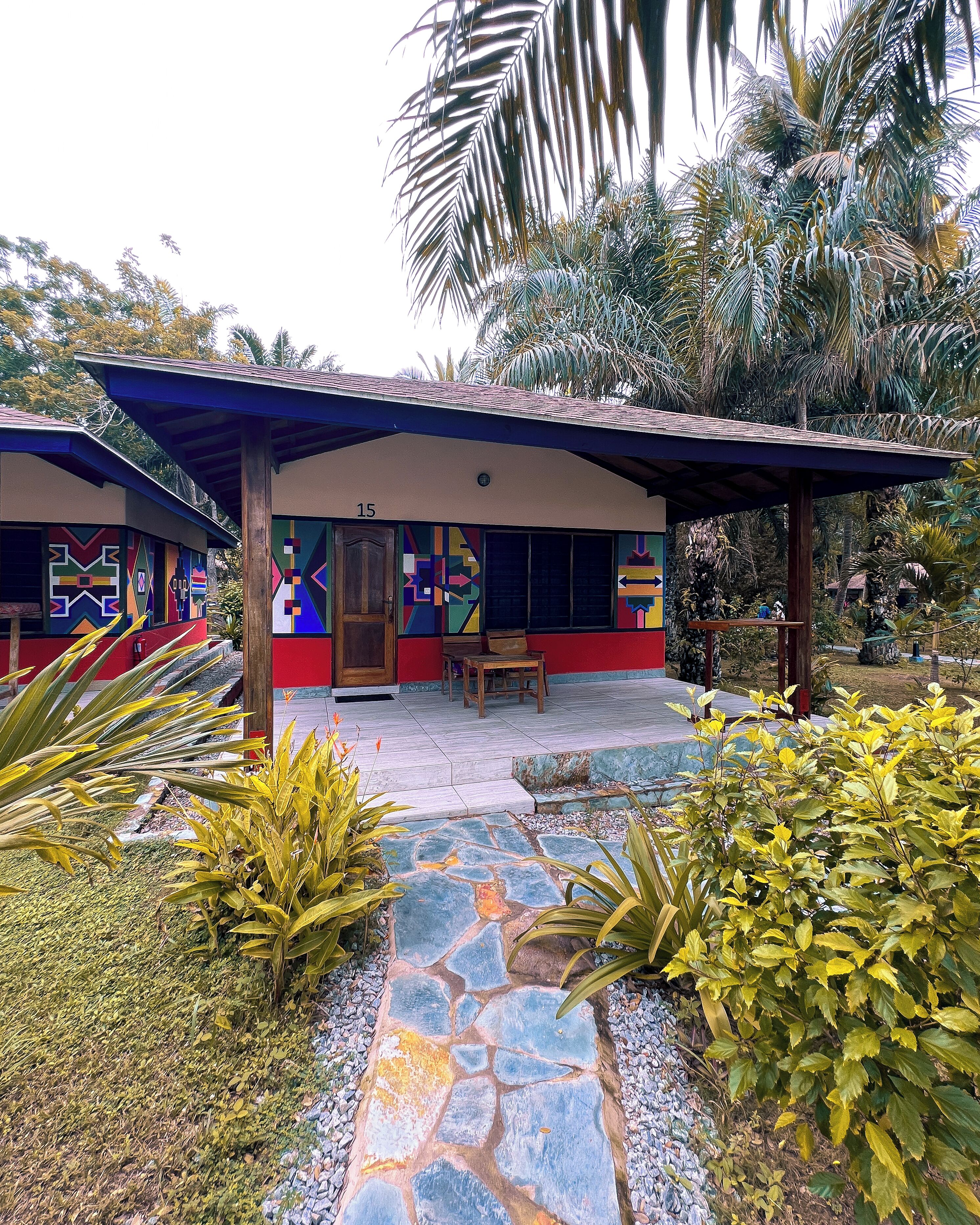 A building with colorful geometric patterns on the walls, a stone pathway, and surrounding tropical vegetation.
