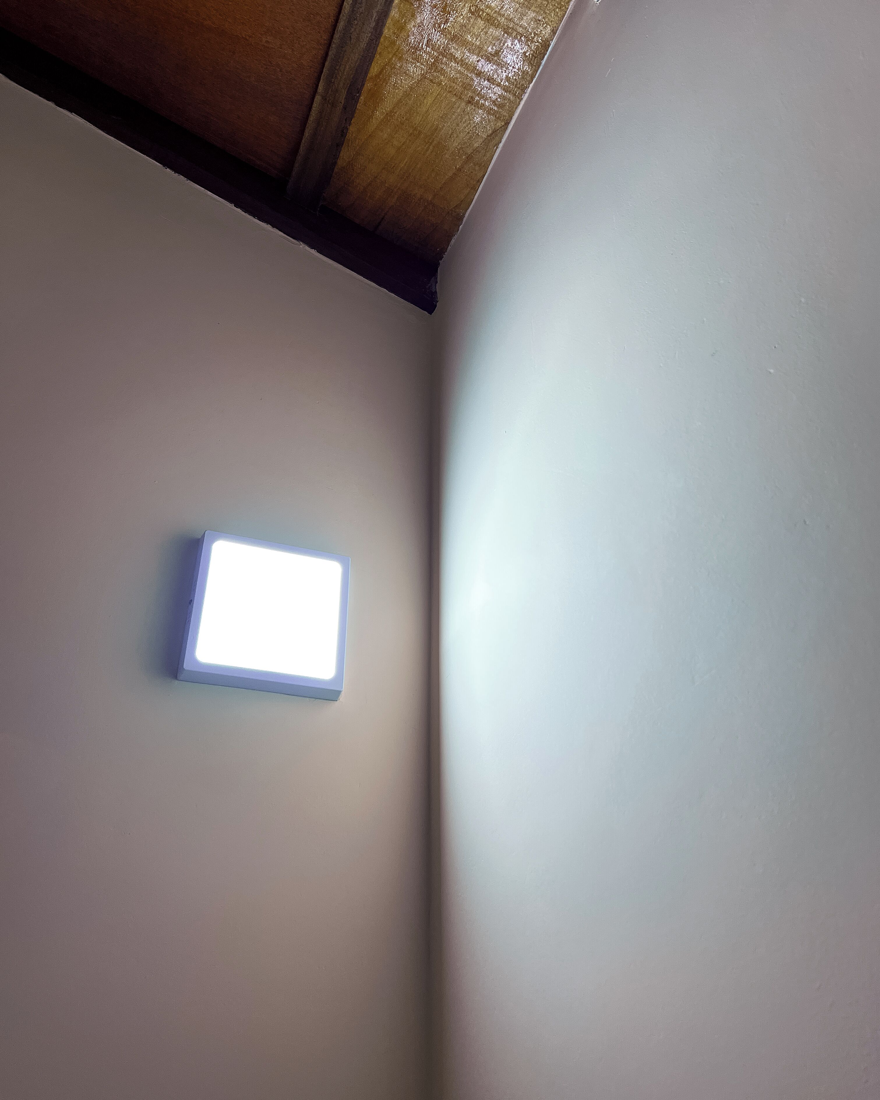 A ceiling with a recessed light fixture and a wooden beam.