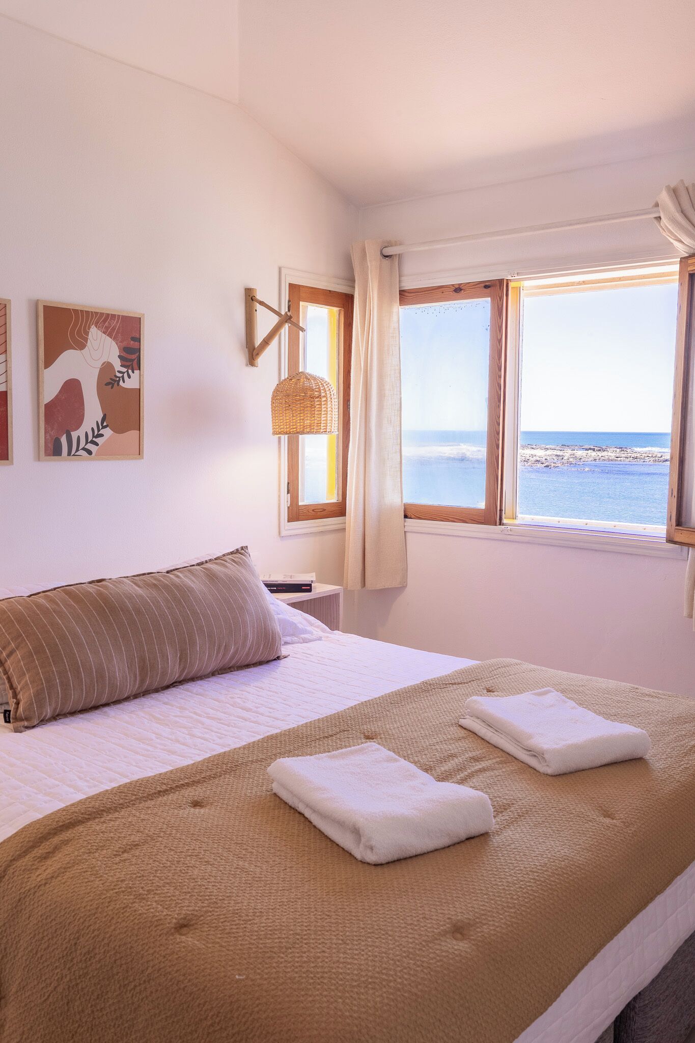 Quarto com cama grande, vista para o mar e luminária na parede.