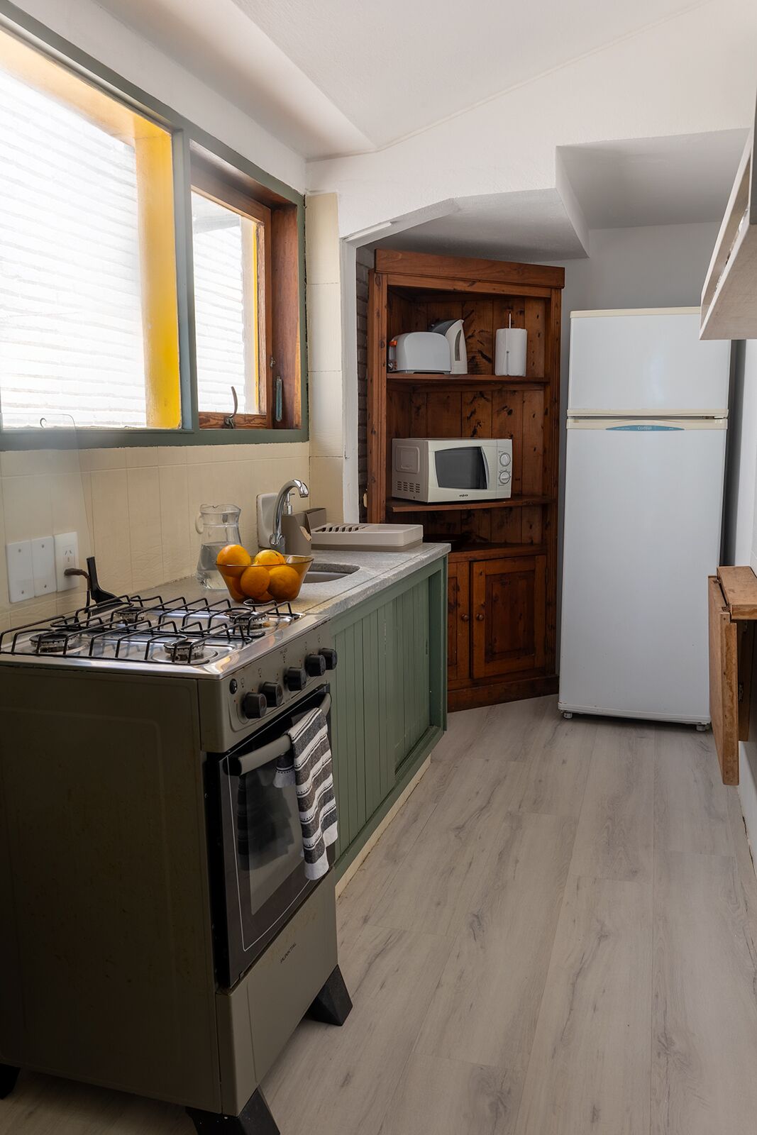 Une cuisine compacte équipée d’une cuisinière à gaz, d’un four et d’un micro-ondes, le tout installé sur une étagère en bois.
