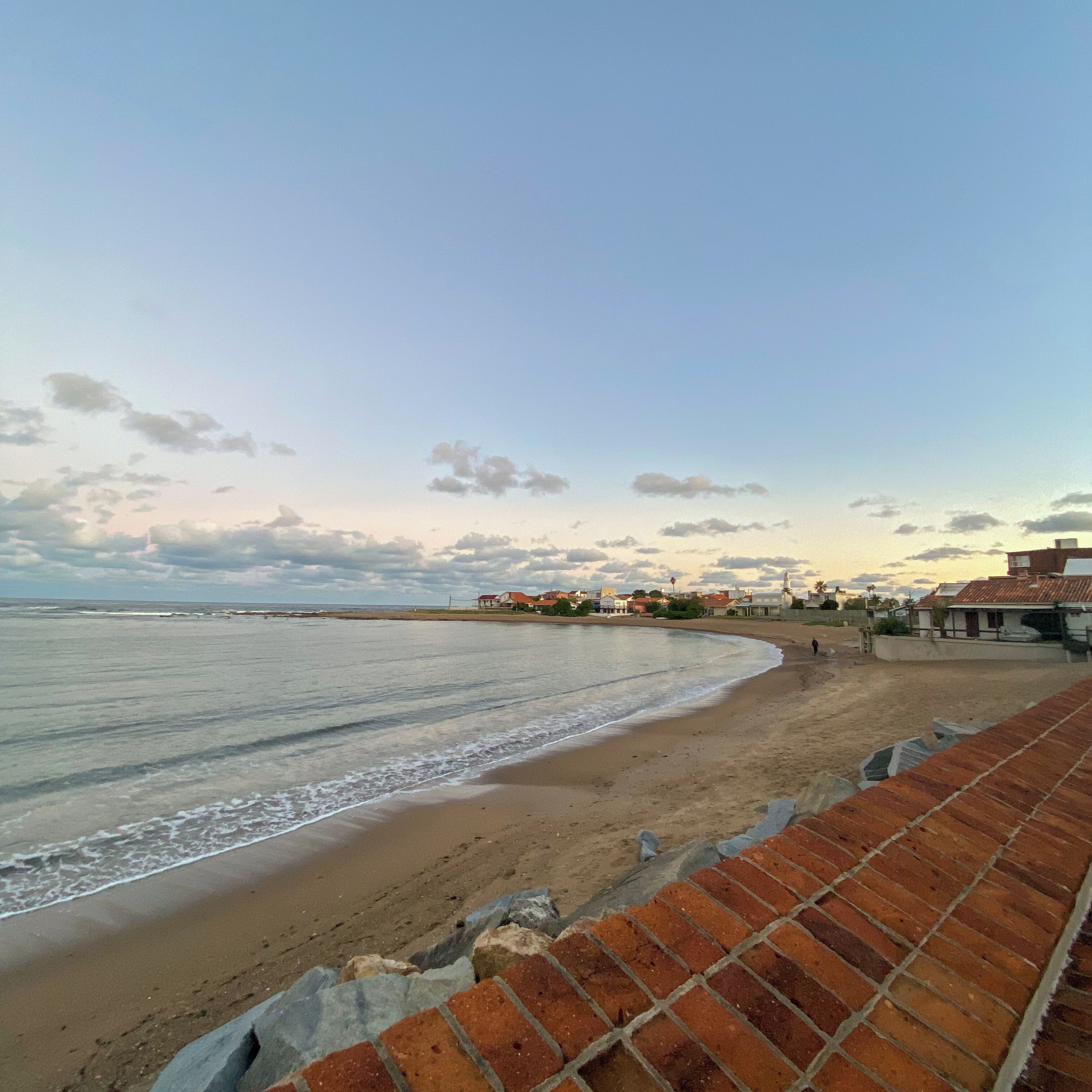 A beach with a brick wall and a row of houses in the background.