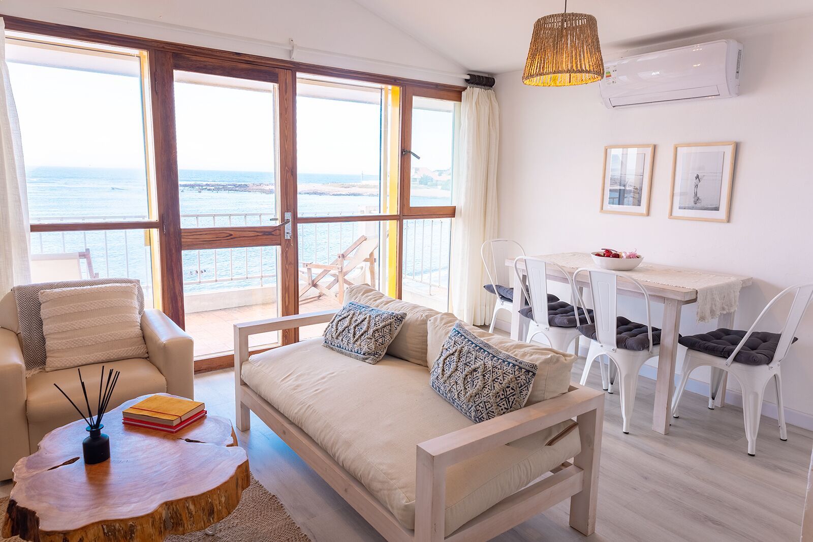 A spacious living area with a sofa, chairs, a dining table, and a view of the sea through large windows.
