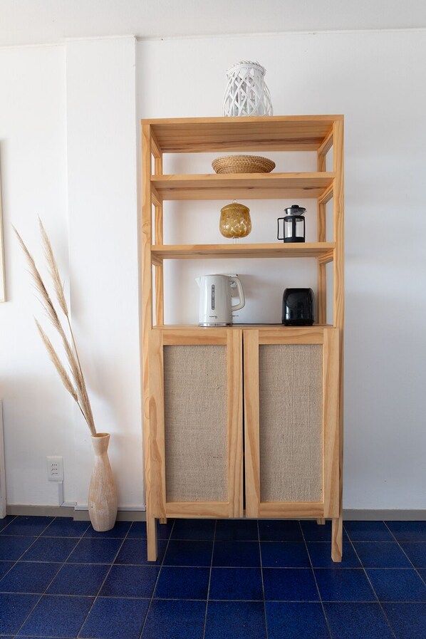 A wooden shelf unit with a woven basket, a glass vase, a coffee maker, and a kettle. - Apartamentos Alborada (La Paloma)