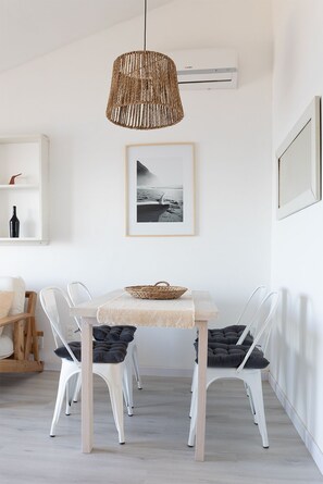 A dining area with a light-colored table, white chairs, a woven pendant light, and a framed black and white photograph on the wall. - Apartamentos Alborada (La Paloma)
