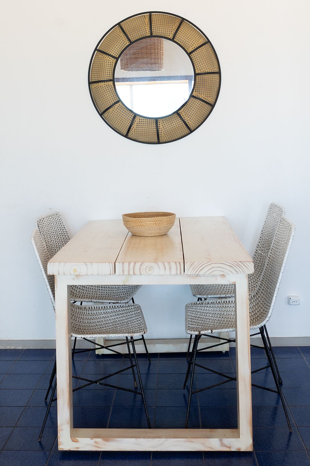 A wooden table with a woven bowl, two wicker chairs, and a circular mirror on the wall.