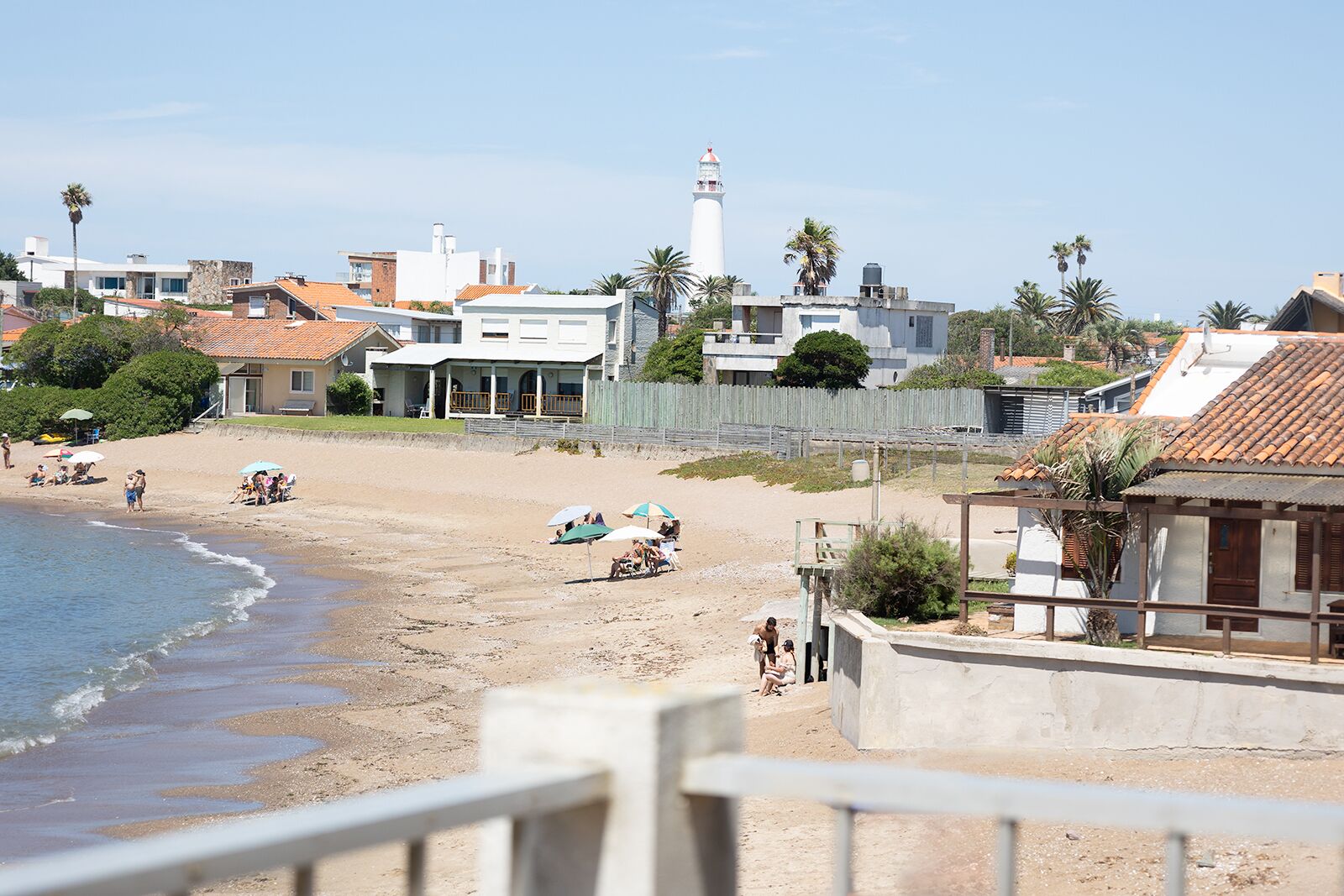 Une plage avec un phare, des maisons et une clôture en bois.